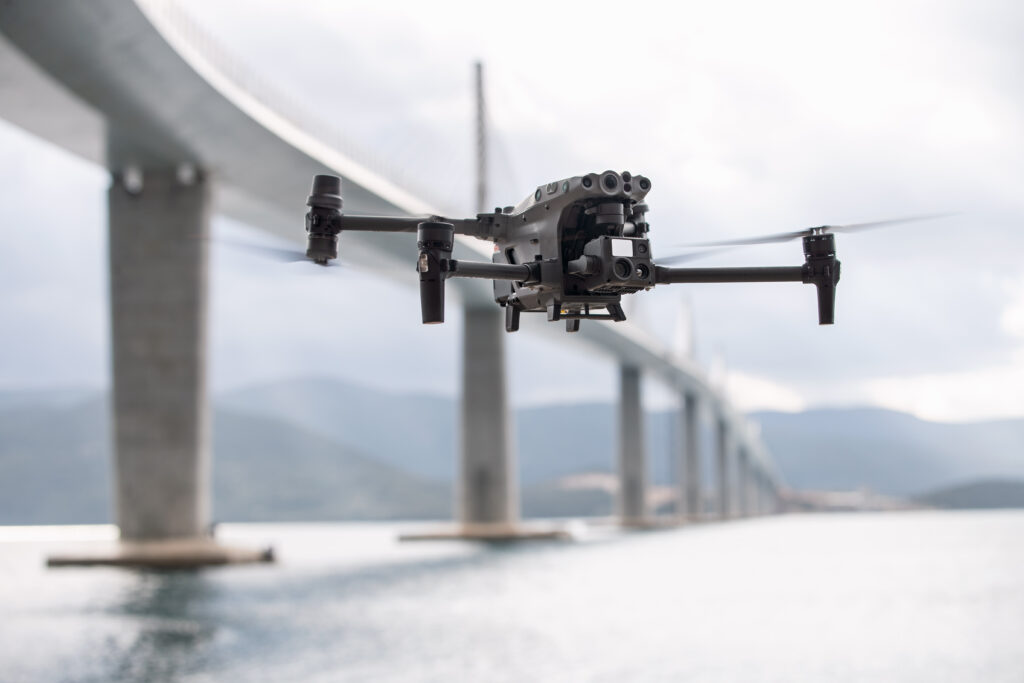 Drohne fliegt vor einer langen Brücke über dem Wasser
